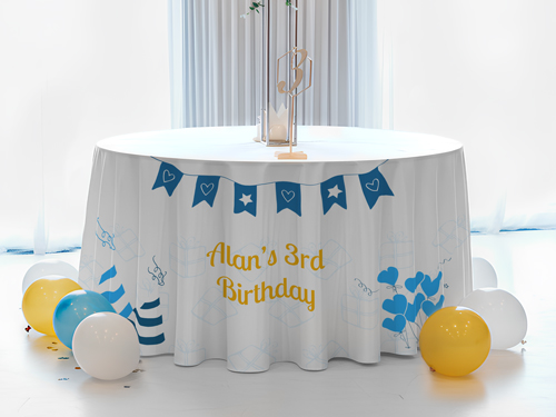 A white, blue, and yellow round table cover with the birthday boy's name and age, with balloons on the floor.