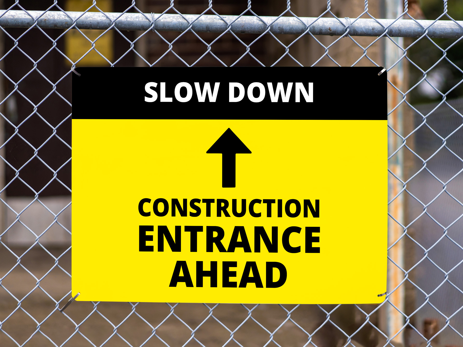A slow down, construction area entrance ahead sign on a chain link fence.