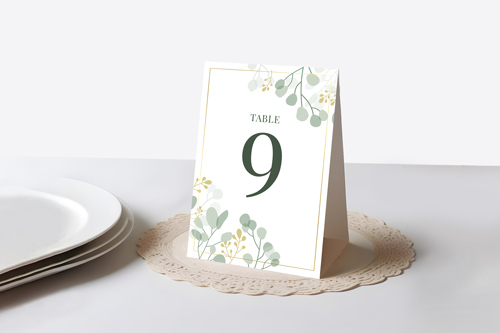Table number 9 card with green and yellow floral design on a lace doily on a white table.