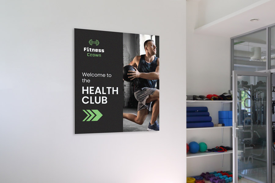 A dark colored wall mounted pvc sign welcoming gym-goers to the health club and showing them the way to the entrance.