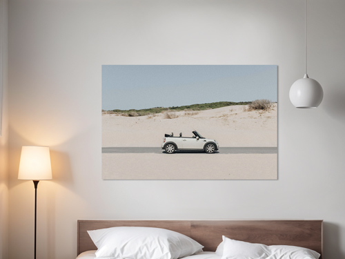 A photo of a convertible on an open road printed on wrapped canvas hanging over a hotel room bed.