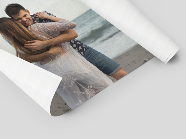 Rolled canvas print of couple embracing on beach, partially unrolled on white surface.