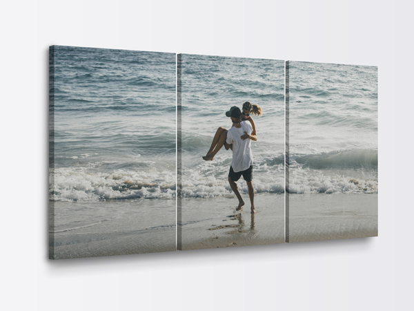 A three panel canvas print of a couple at the ocean shore, man carrying woman on the beach.