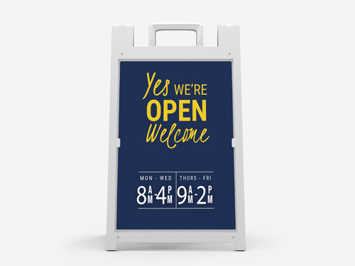 Real estate sandwich board featuring a welcoming message and open hours.